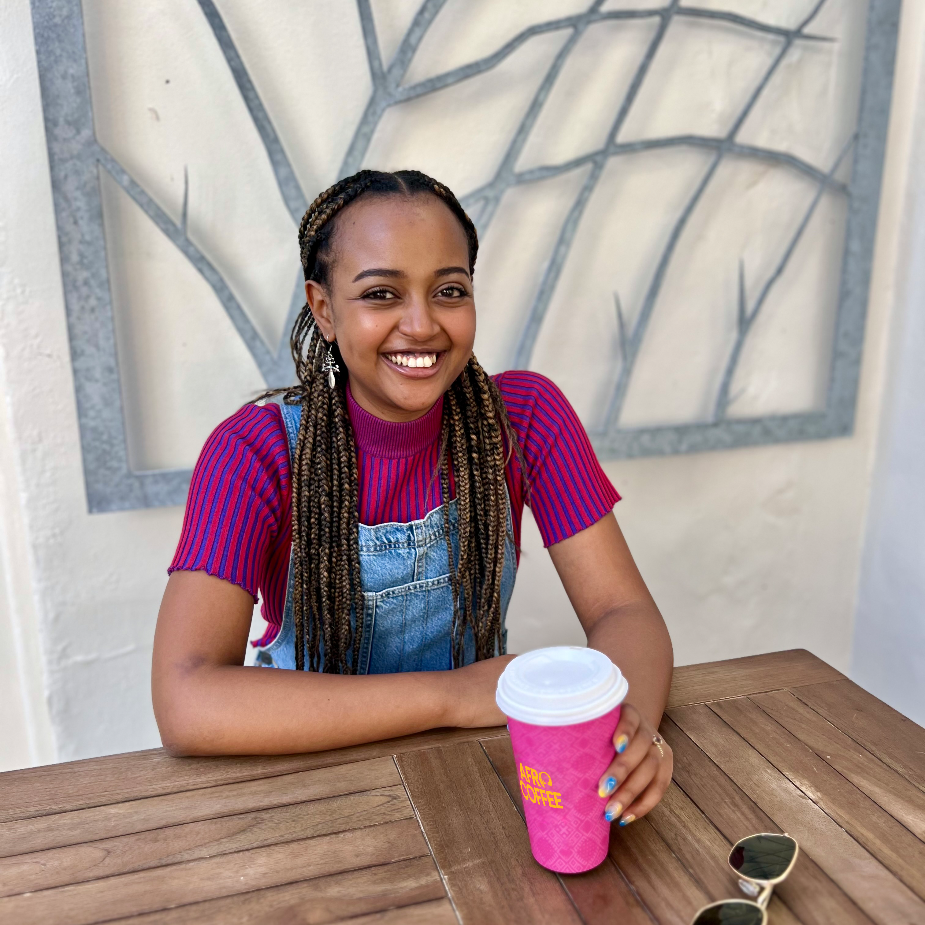 Sitzende Frau auf einem Tisch, die einen Afro Coffee Cup in der Hand hält. 