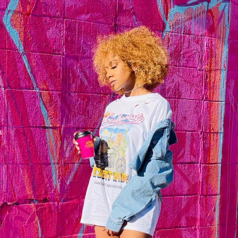 Frau vor einem pinken Hintergrund mit Afro Coffee Cup in der Hand. 